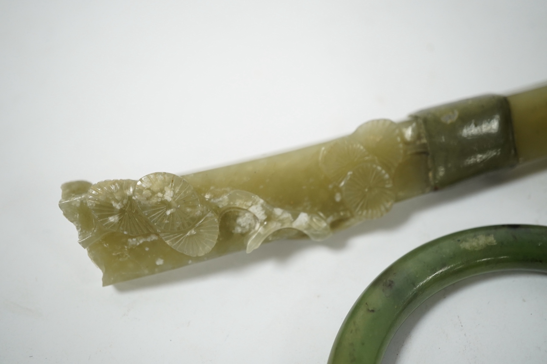 A Chinese celadon jade ruyi sceptre (incomplete) and a spinach jade bangle, late Qing, largest 15.5cm in length (2). Condition - bangle good